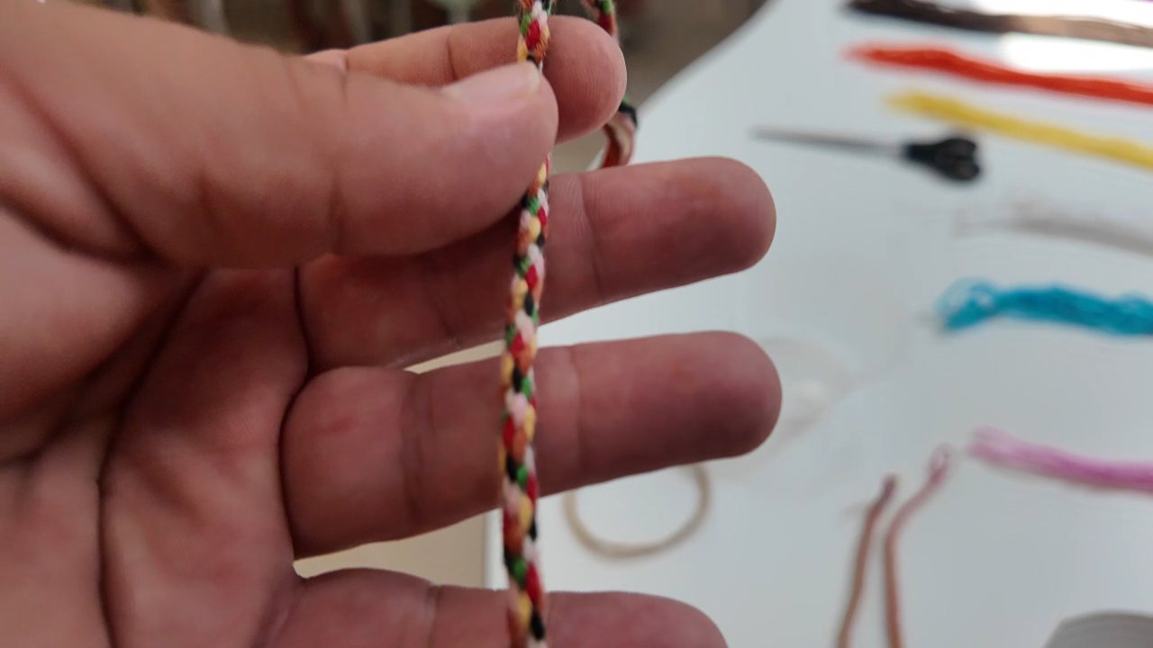 Cordón redondo de una pulsera de hilo visto de cerca en la mano, con los colores cruzándose en espiral