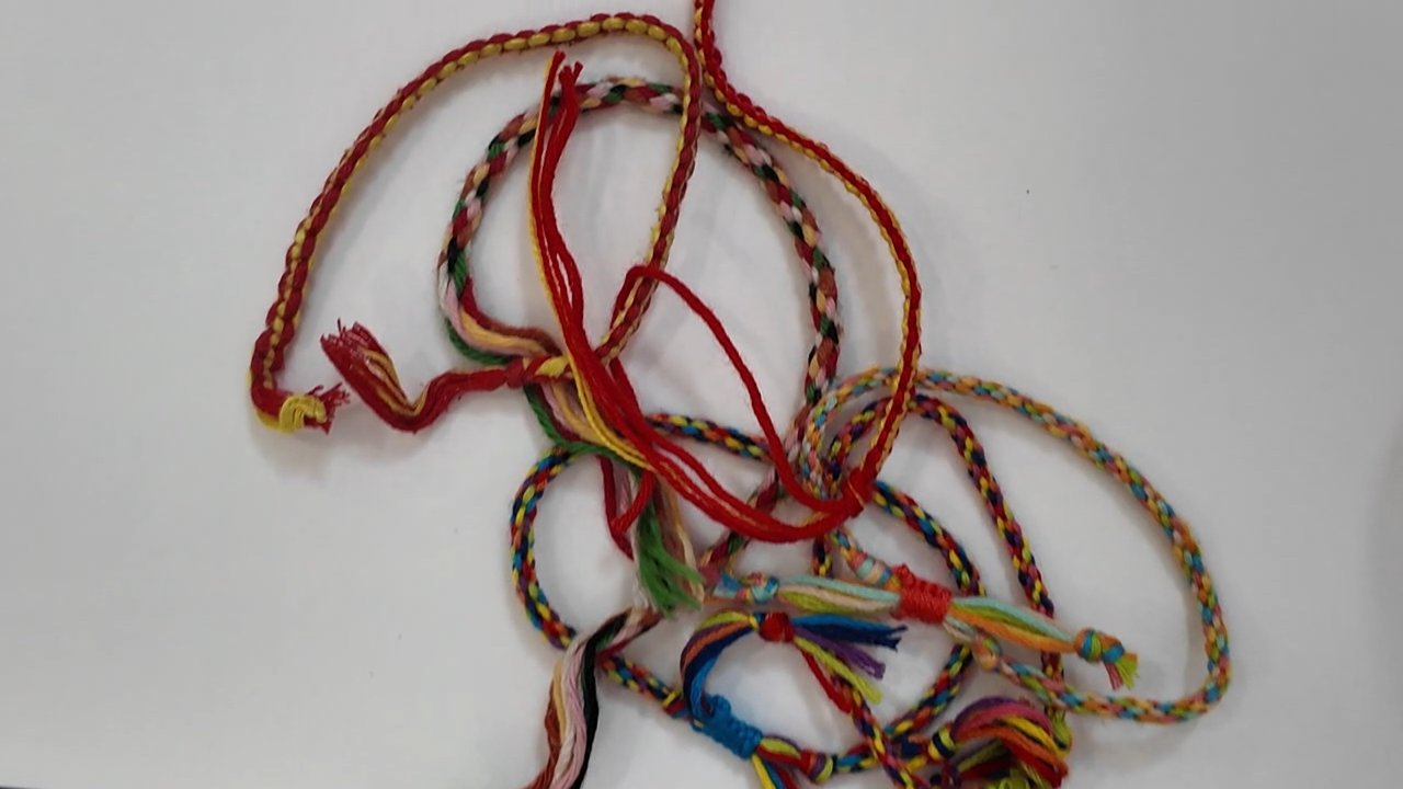 Pulseras de hilo terminadas sobre una mesa blanca: cordones redondos de varios colores, con los flecos de los nudos en las puntas