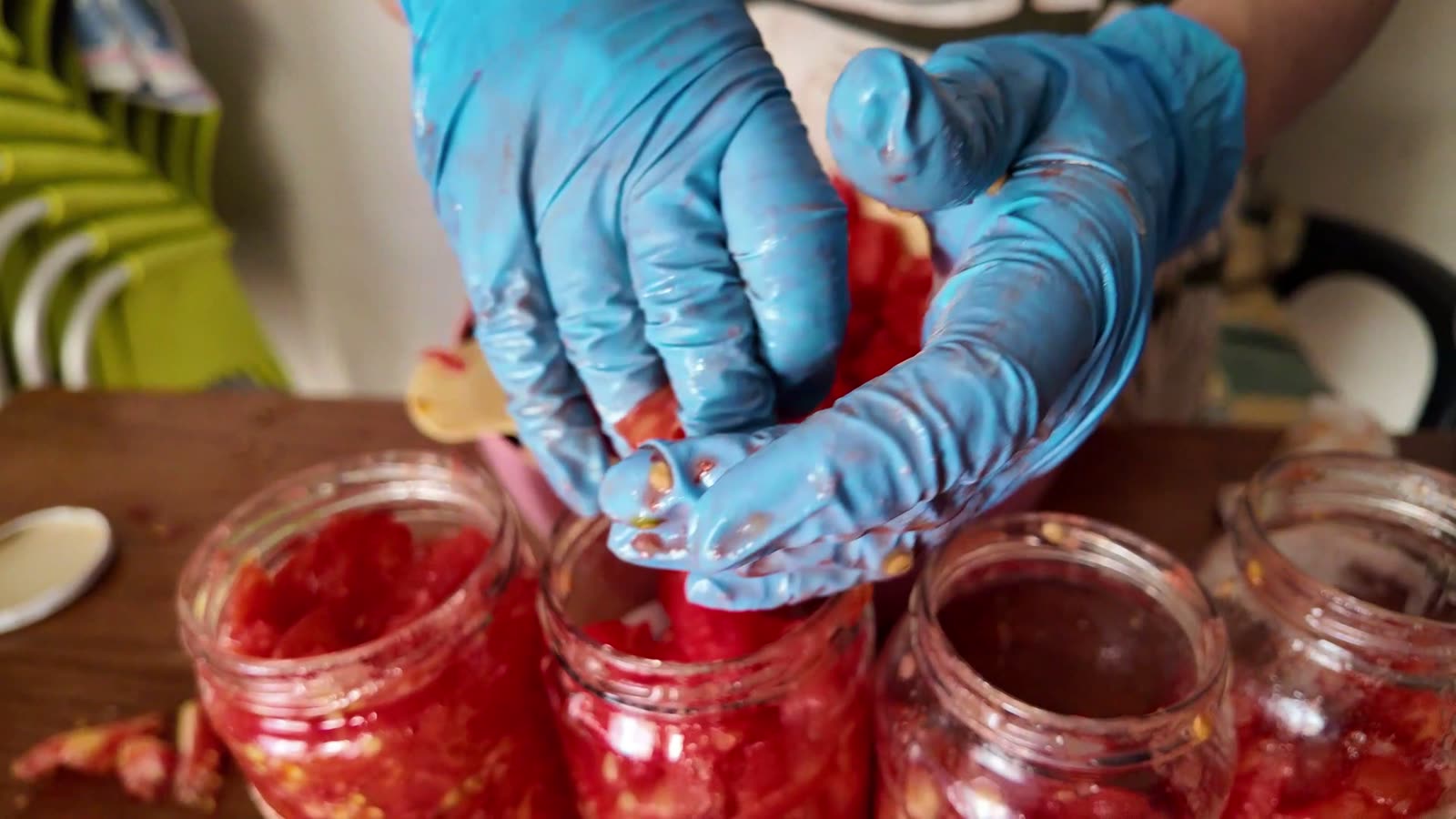 Manos con guantes metiendo tomate troceado en un bote de cristal y apretándolo para que no quede aire